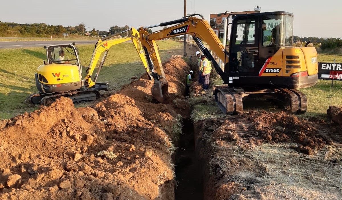 Dos retroexcavadoras abriendo una zanja para fibra óptica junto a una ruta