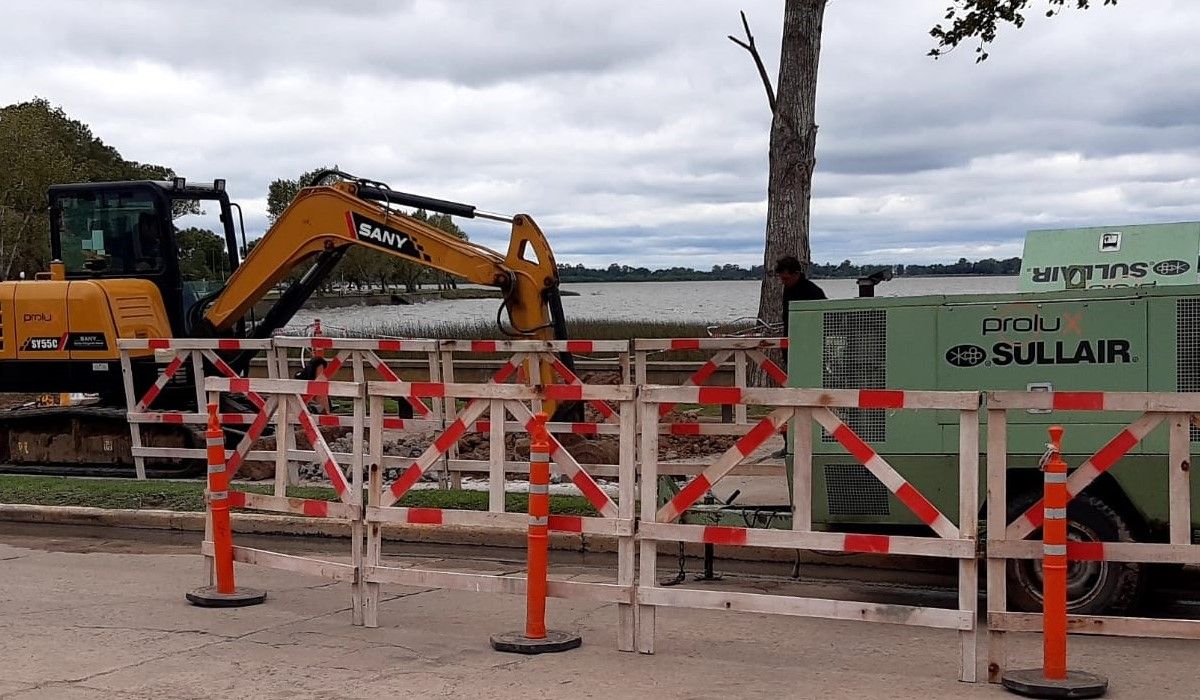 Retroexcavadora trabajando detrás de vallas de obra junto a un lago