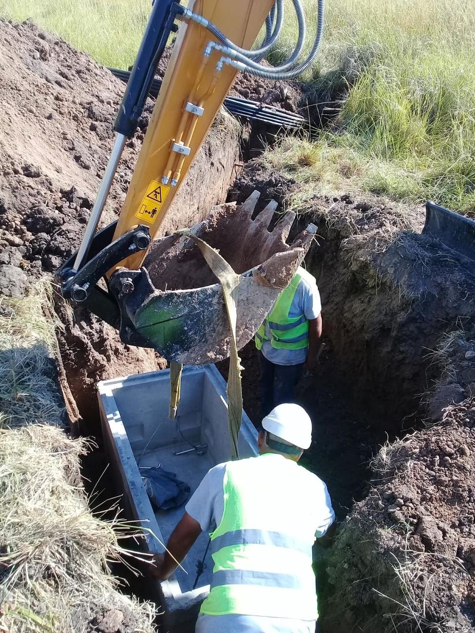 Operarios colocando una cámara de hormigón en una zanja con una retroexcavadora